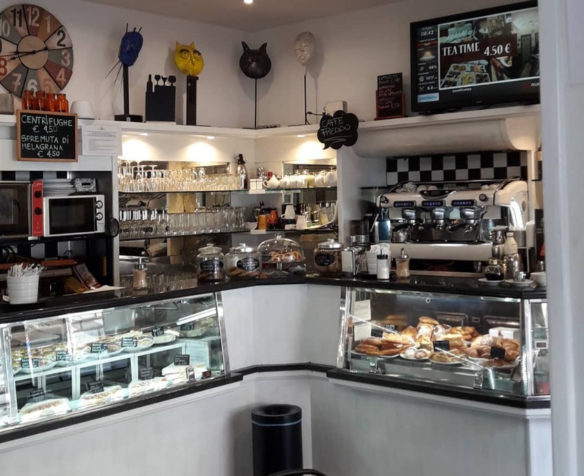 Banco del Simon Bar con vetrine di cornetti e panini, macchina da espresso e lavagna «Centrifughe € 4,50